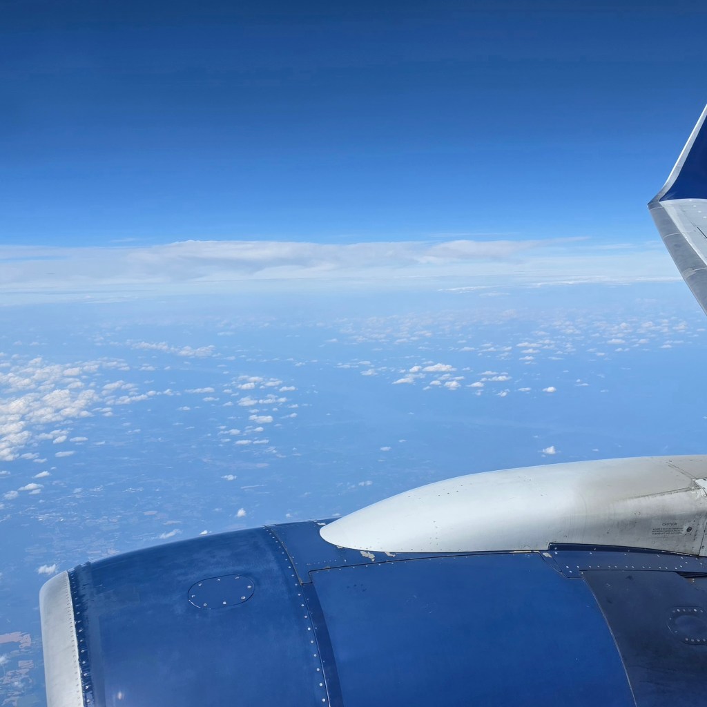 picture taken from the window seat of an airplane. blue skies, clouds, and earth below. 